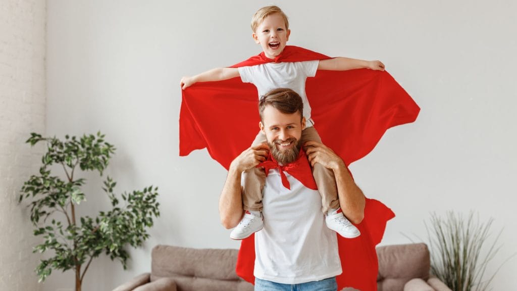 bearded dad with cape carrying child on shoulders